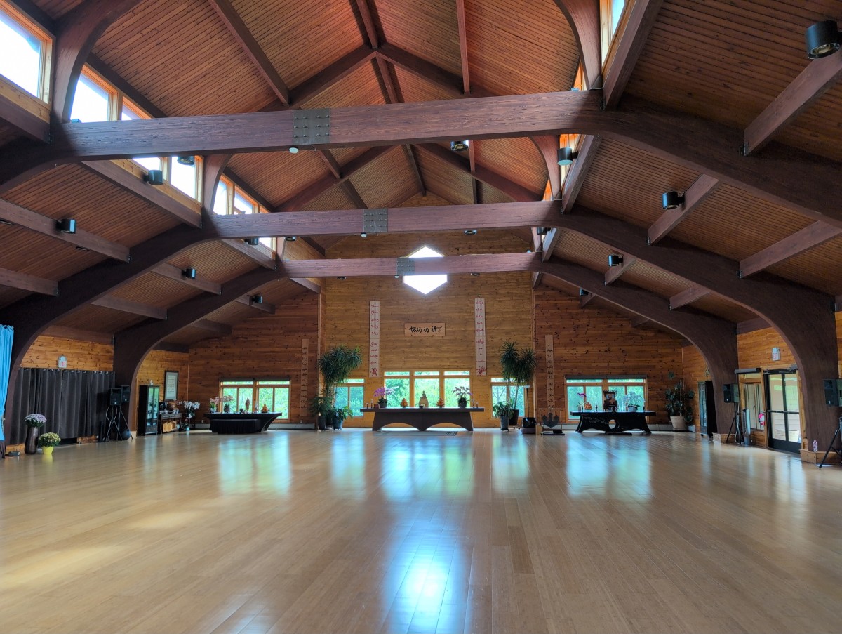 Huge meditation hall where people meditate. It's a huge wooden structure and the wood looks beautiful and clean.