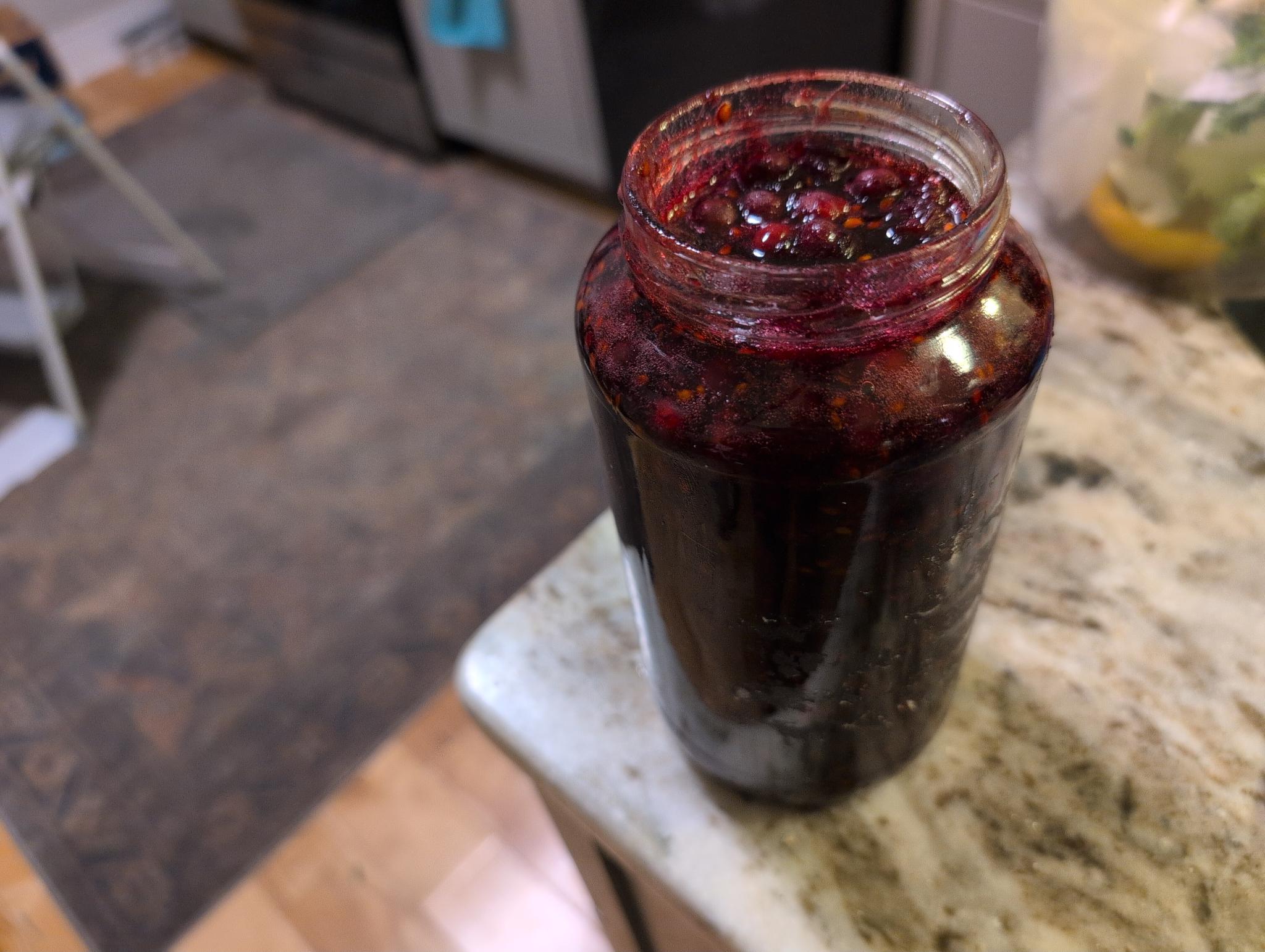 A bottled juneberry jam. It has a deep red color and it fills the jar to the brim.
